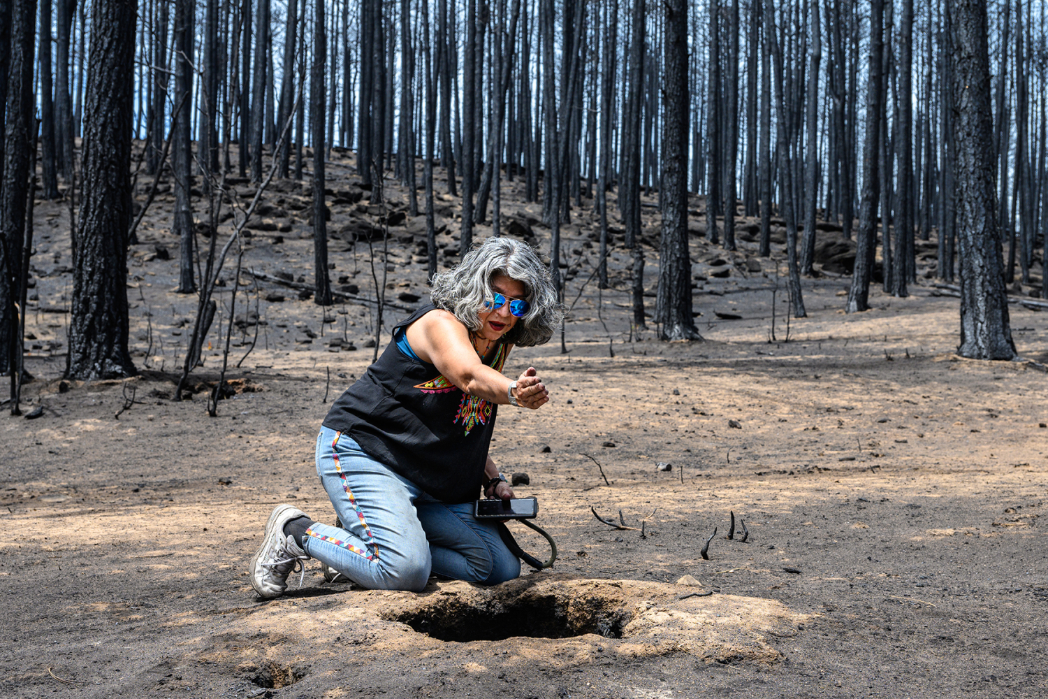 Pola Lopez sits by a hole where a ponderosa pine was vaporized by the Hermits Peak/Calf Canyon fire, noting the underground root tunnels leading away from it. Michael Benanav/Searchlight New Mexico