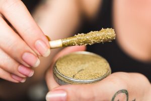 Woman holding a cannabis or marijuana joint in her hand. Joint is dipped in oil or wax and sprinkled with kief (THC powder)